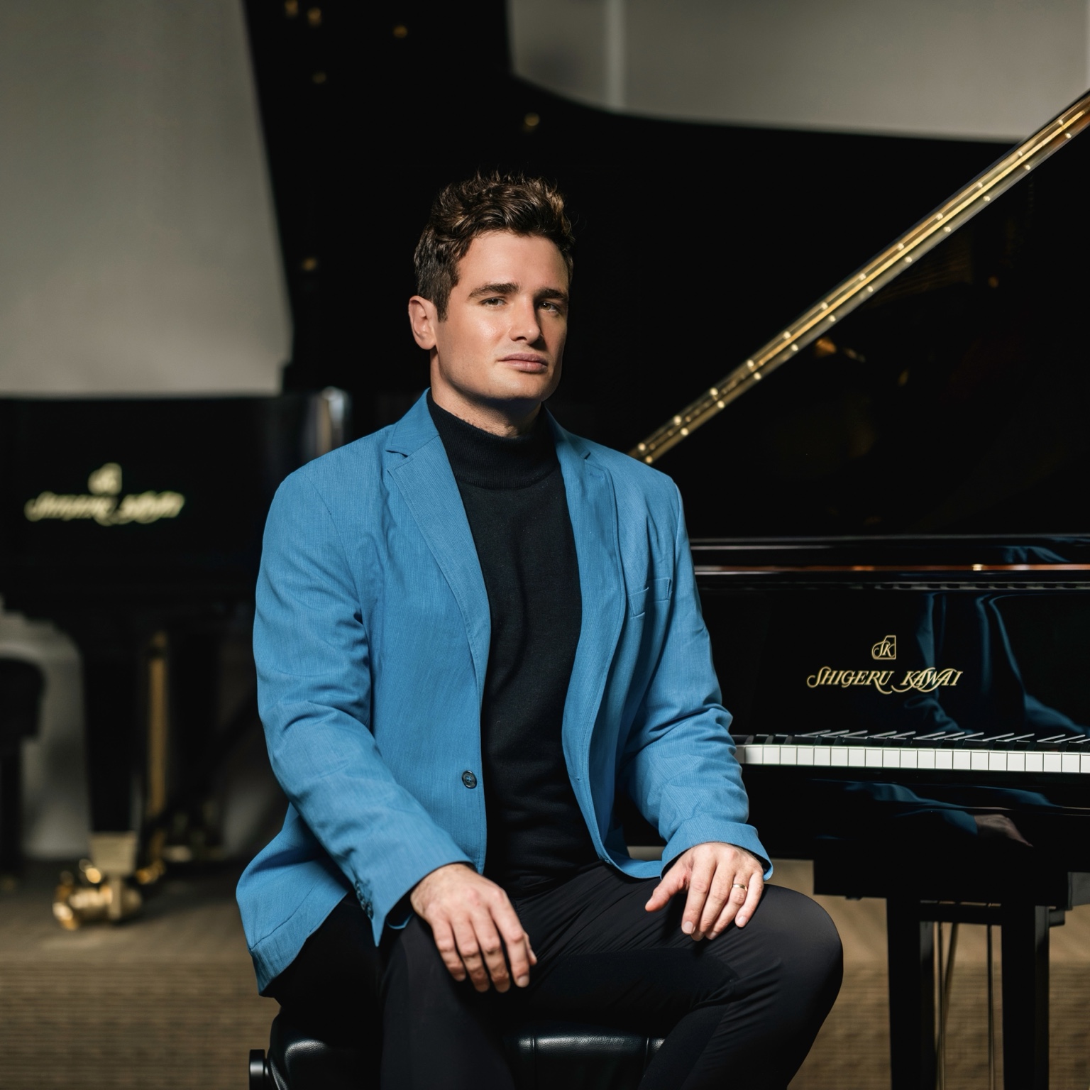 Artem Kuznetsov in a blue jacket beside a Shigeru Kawai piano