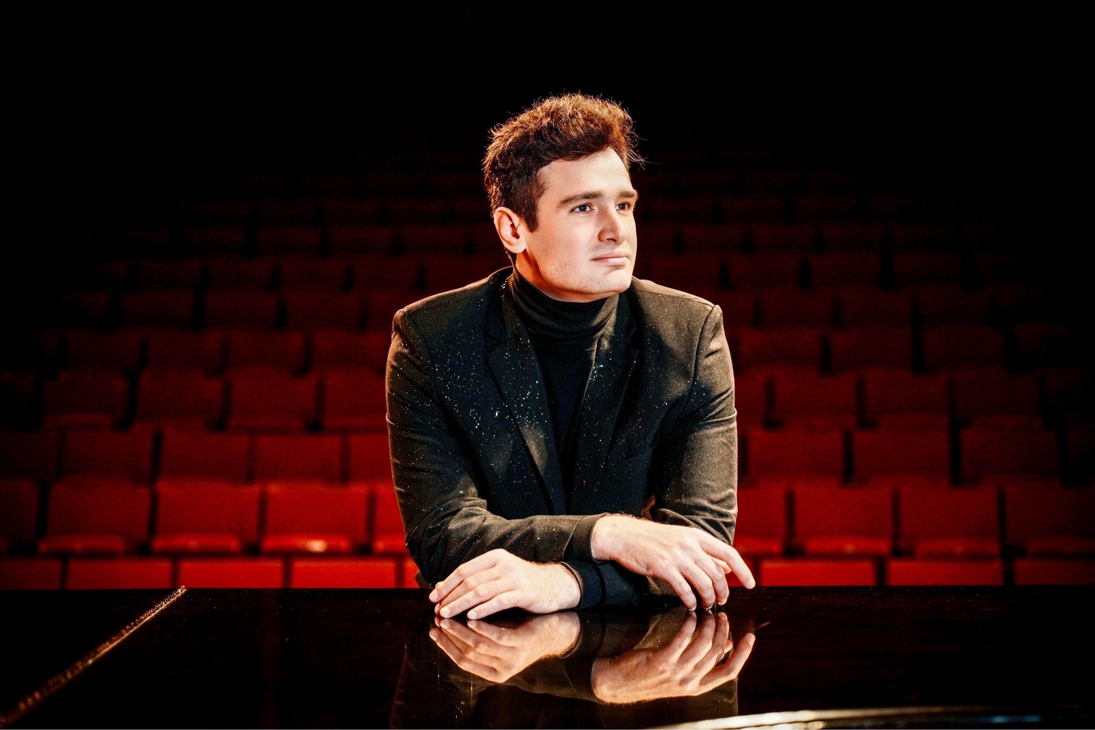 Artem Kuznetsov seated at a piano in a red concert hall